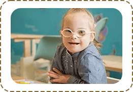 A young girl with glasses sitting in front of a wall.