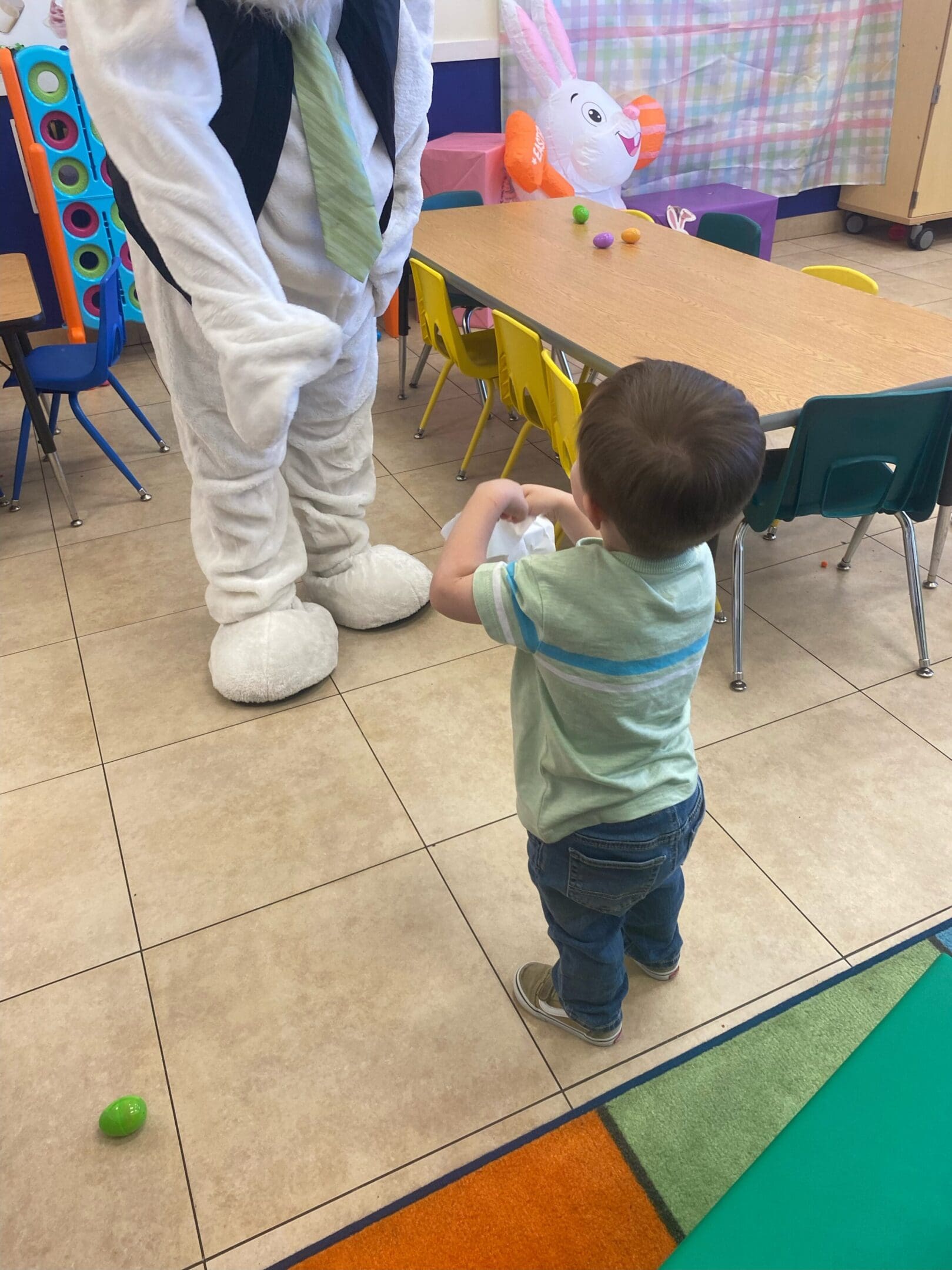 A toddler standing next to an adult in front of tables.