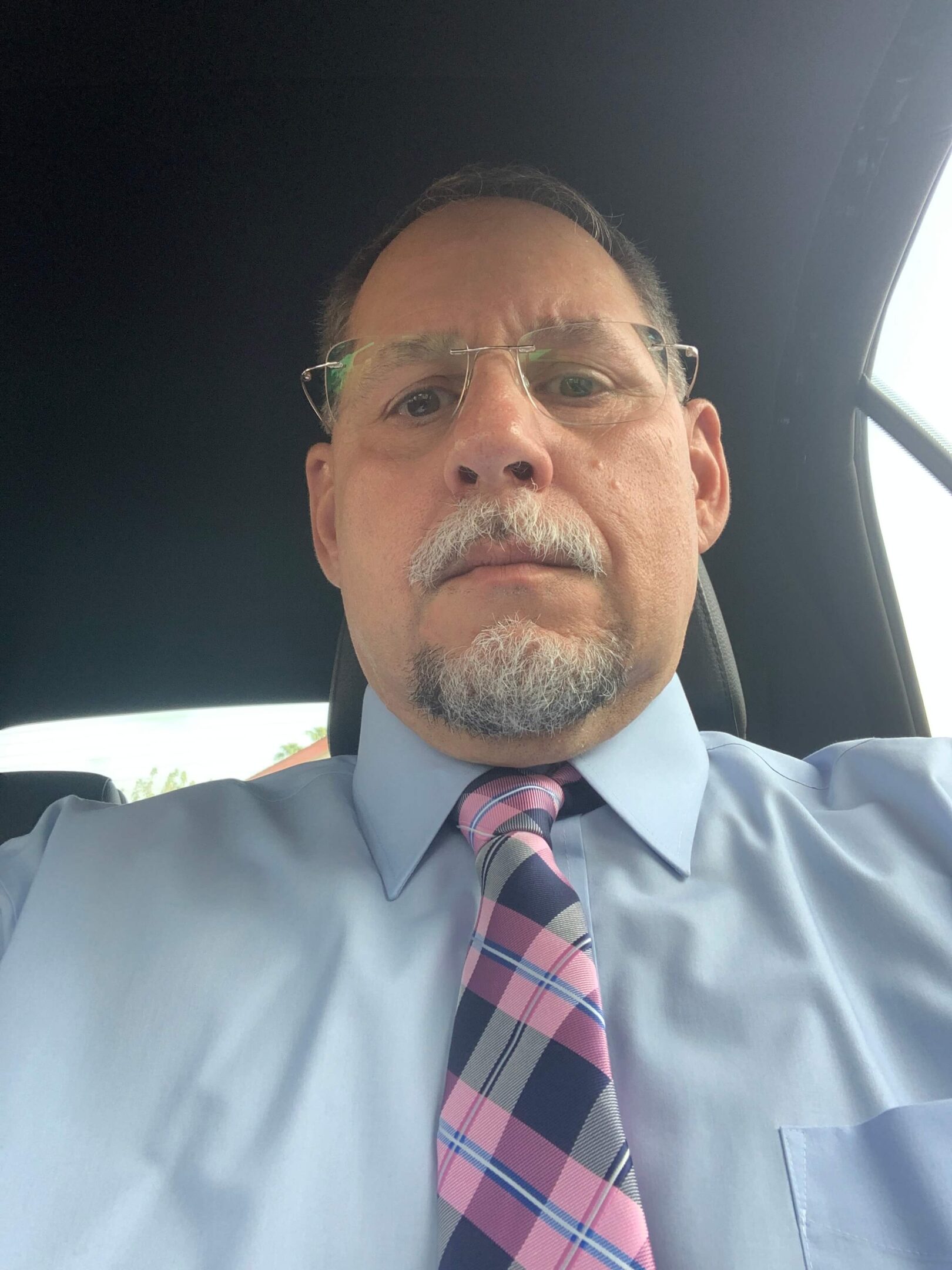 A man in a blue shirt and tie sitting inside of a car.