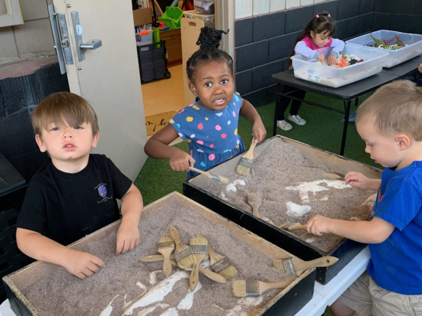 Three children are playing with clay in a classroom.