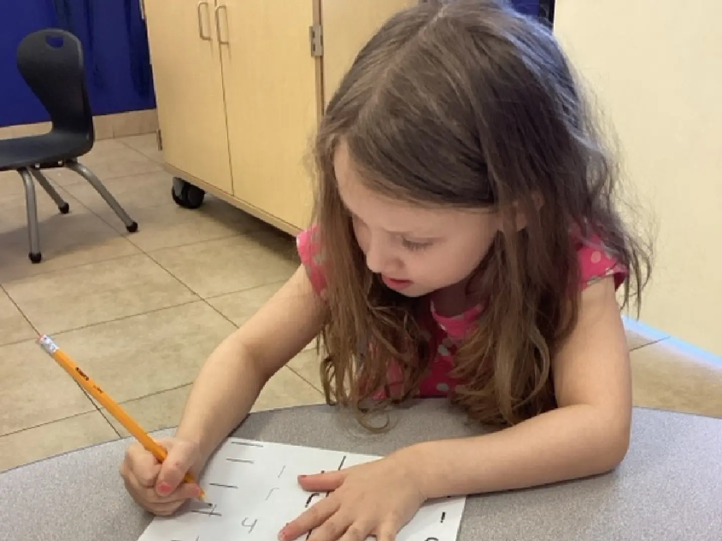 A little girl is writing on paper with a pencil.